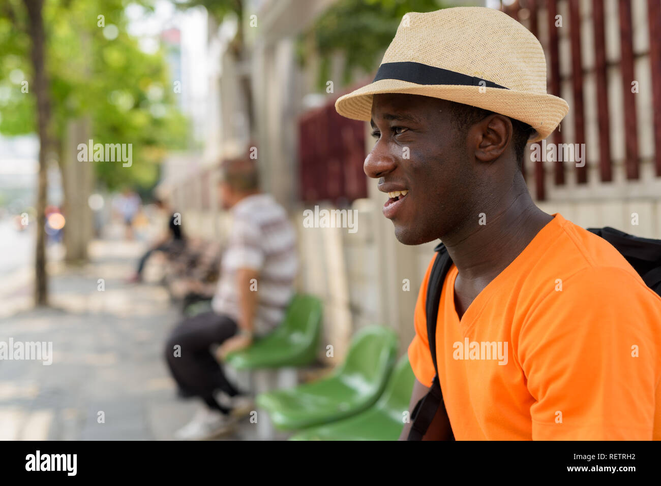 Junge glücklich schwarzen Afrikanischen touristische Mann an der Bushaltestelle sitzen Stockfoto