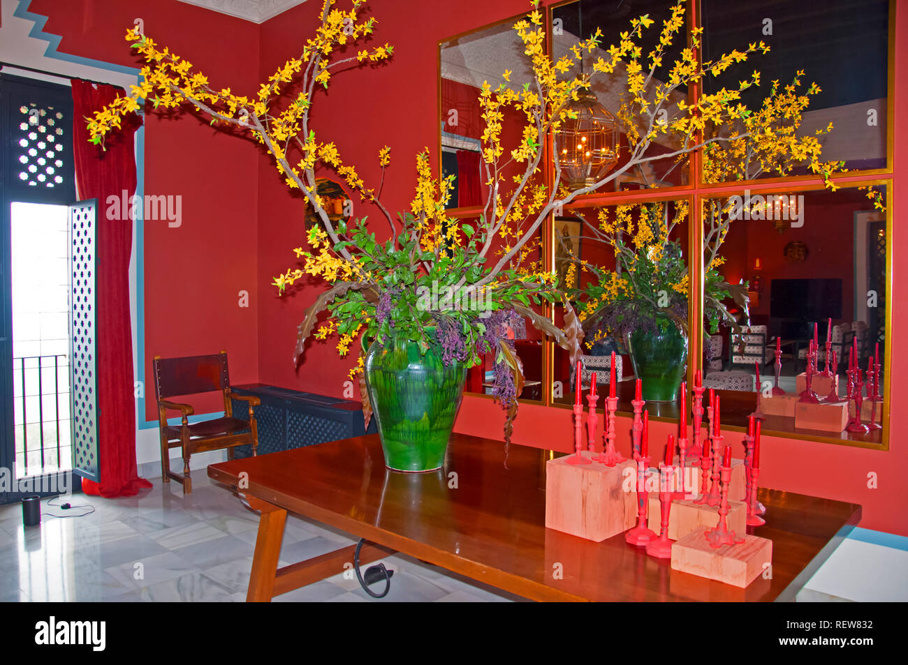 Große grüne Vase mit gelben Blüten und rote Kerzen auf dem Tisch, Spiegel an der Wand, Boden, Rot innen Marvel Stockfoto