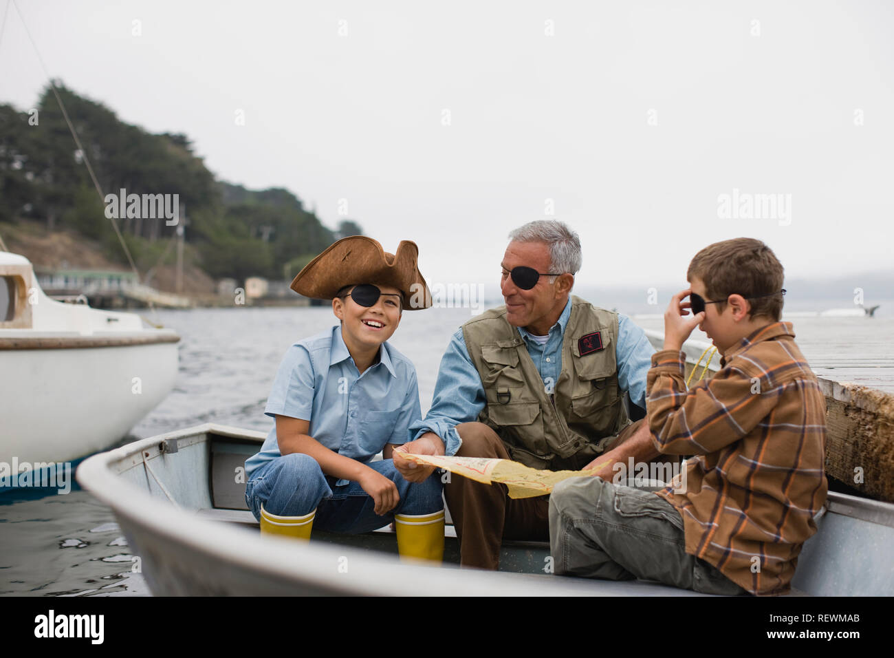 Vater sitzt in einem Ruderboot mit seinen beiden Söhnen gekleidet als Piraten. Stockfoto