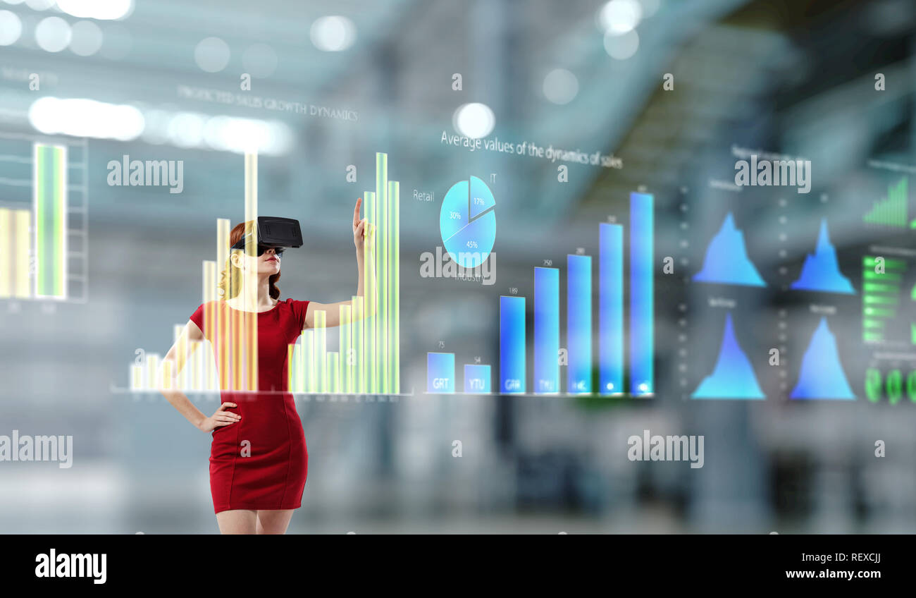 Attraktive Frau im roten Kleid tragen virtuelle Helm und mit Medien zu arbeiten. Mixed Media Stockfoto