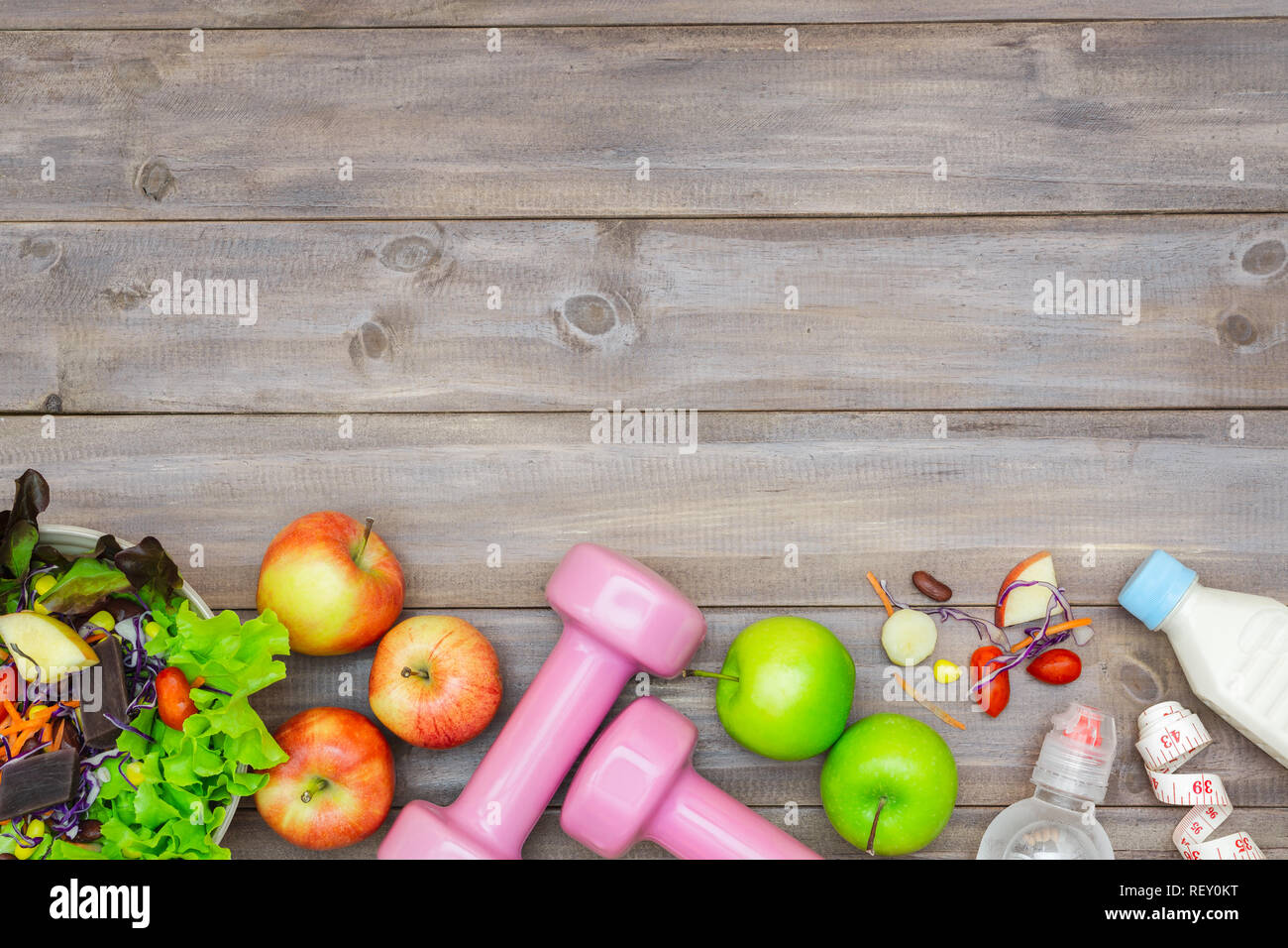 Blick von oben auf die gesunde Lebensweise Konzept, Kurzhanteln, Flasche Wasser, Milch, Äpfel und frische Salat auf Holz Hintergrund. Ansicht von oben mit der Kopie. Stockfoto