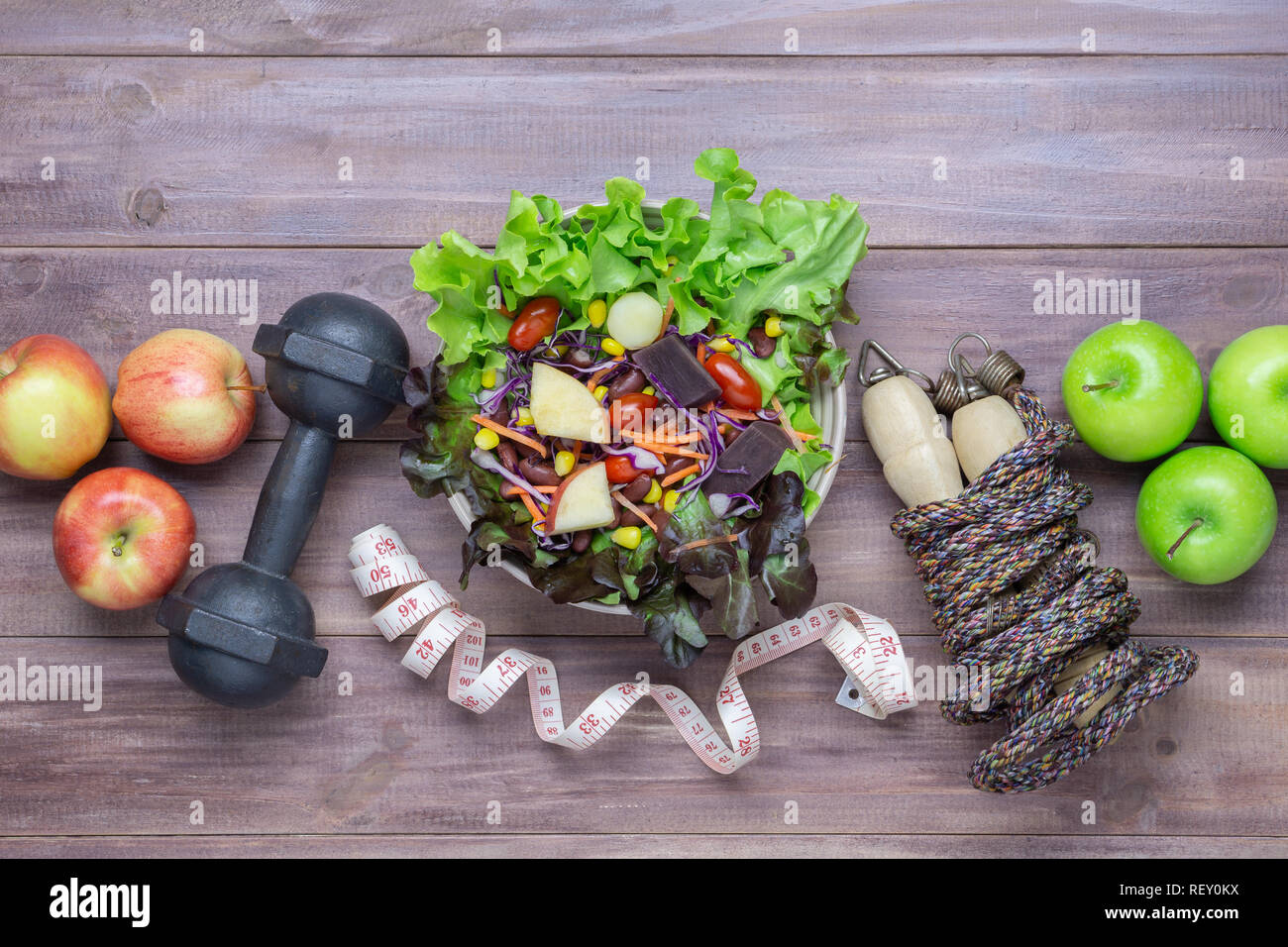 Blick von oben auf die gesunde Lebensweise Konzept, Kurzhanteln, Seil springen, Äpfel und frische Salat auf Holz Hintergrund. Ansicht von oben mit der Kopie. Stockfoto