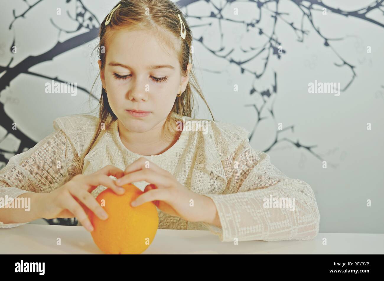 Weiß kaukasischen Girl (Kind, Kind), die Versuchen, eine orange von Hand auszupacken Stockfoto