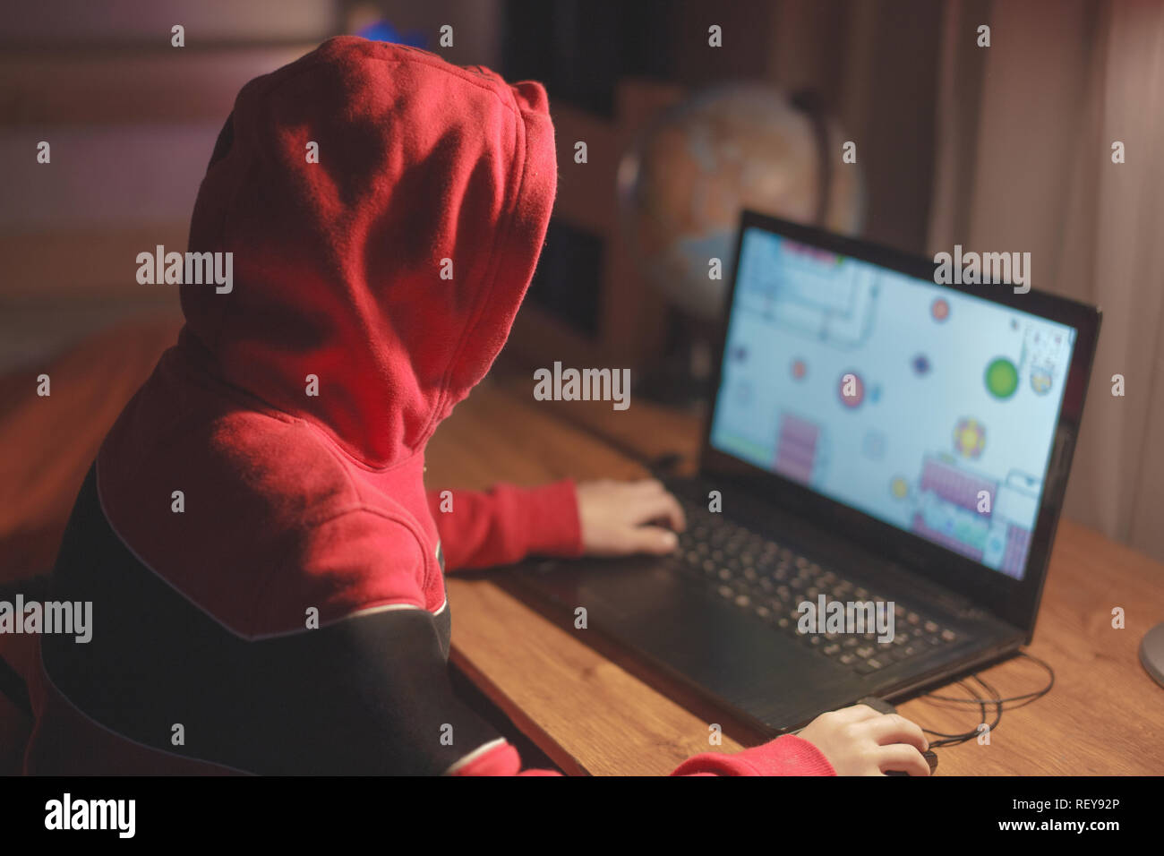 Wenig gamer Kid in der Motorhaube spielen Mass multiplayer spiel online auf Laptop zu Hause während der Nacht Stockfoto