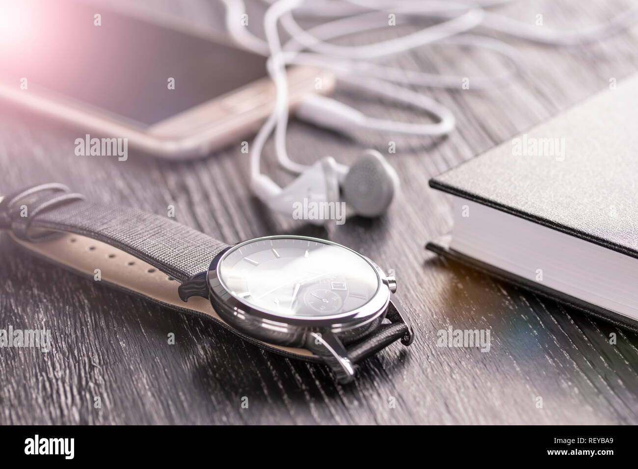 Altes, dunkles Office Desktop mit Elementen für Wirtschaft und Arbeit. Armbanduhr, Handy mit Kopfhörer und Notepad. Das Konzept der schnellen und anhaltenden bu Stockfoto