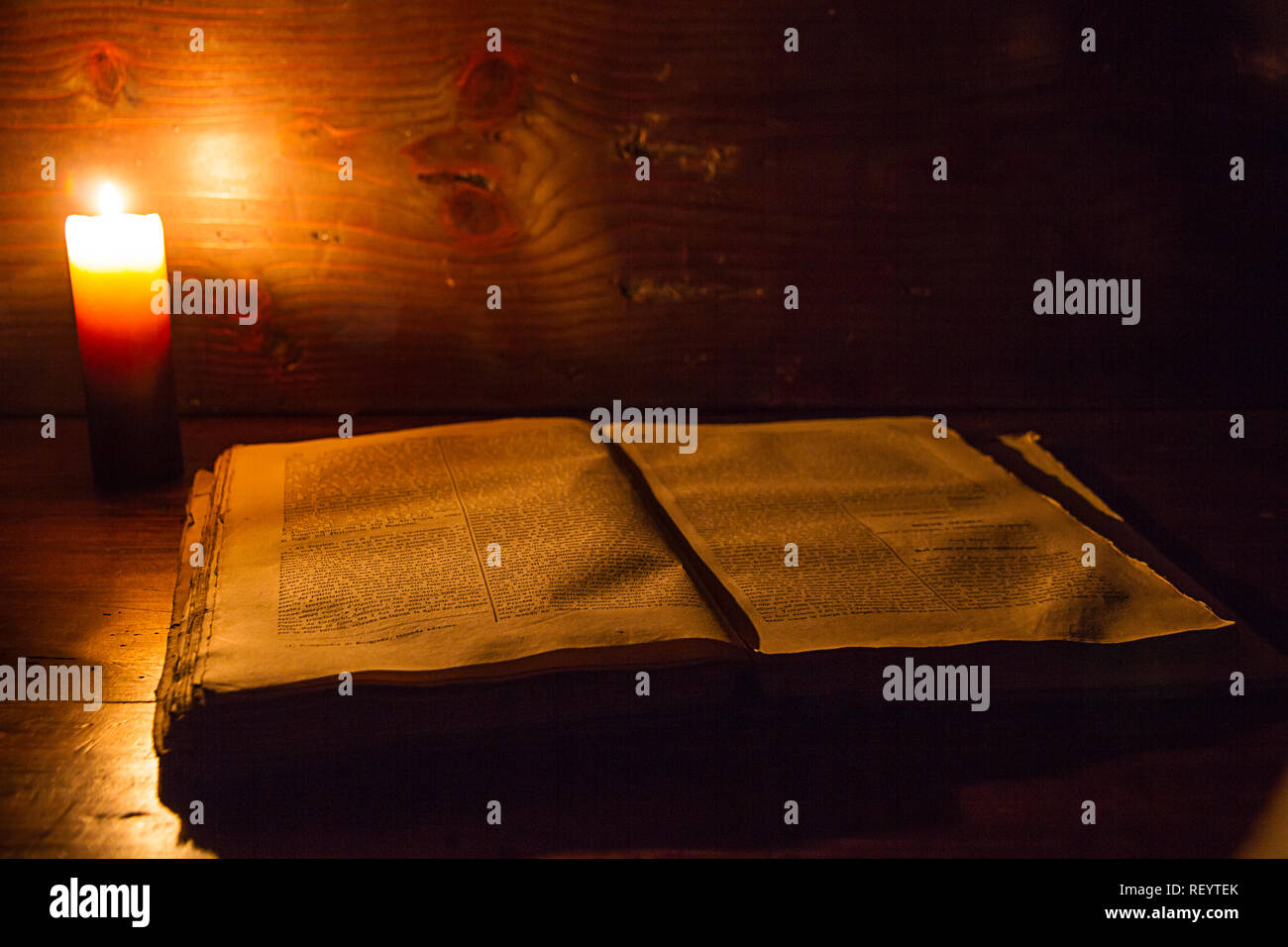 Lesen Szene in alten Zeiten: ein altes Buch lehnte sich auf ruiniert Holztisch beleuchtet durch eine Kerze auf einem hölzernen Hintergrund Stockfoto