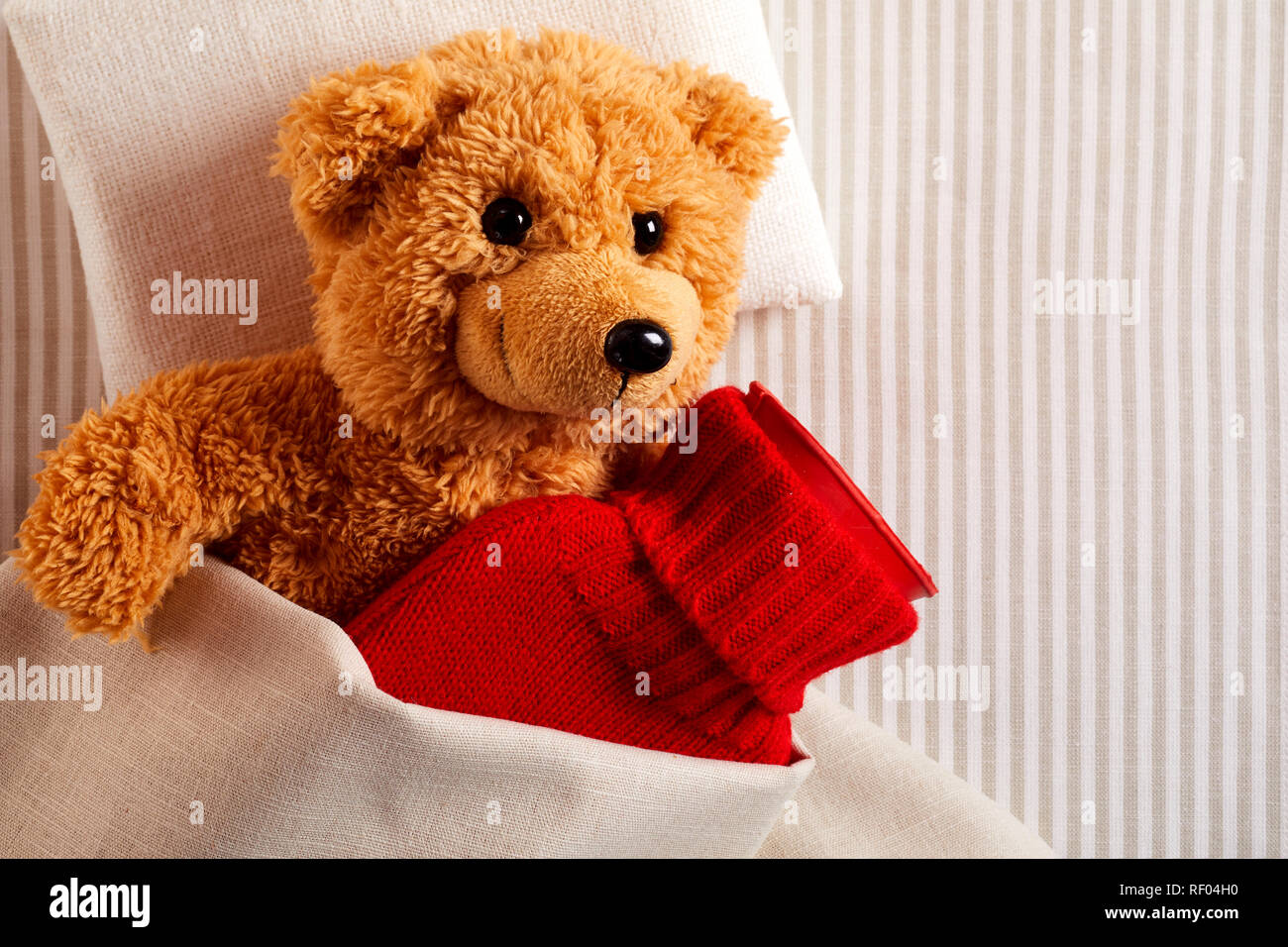 Kranker kleiner Teddybär mit Fieber Kuscheln im Bett mit einer Wärmflasche  in einem hellen Rot gestrickt Abdeckung in einem Konzept der pädiatrischen  Healthcare Stockfotografie - Alamy