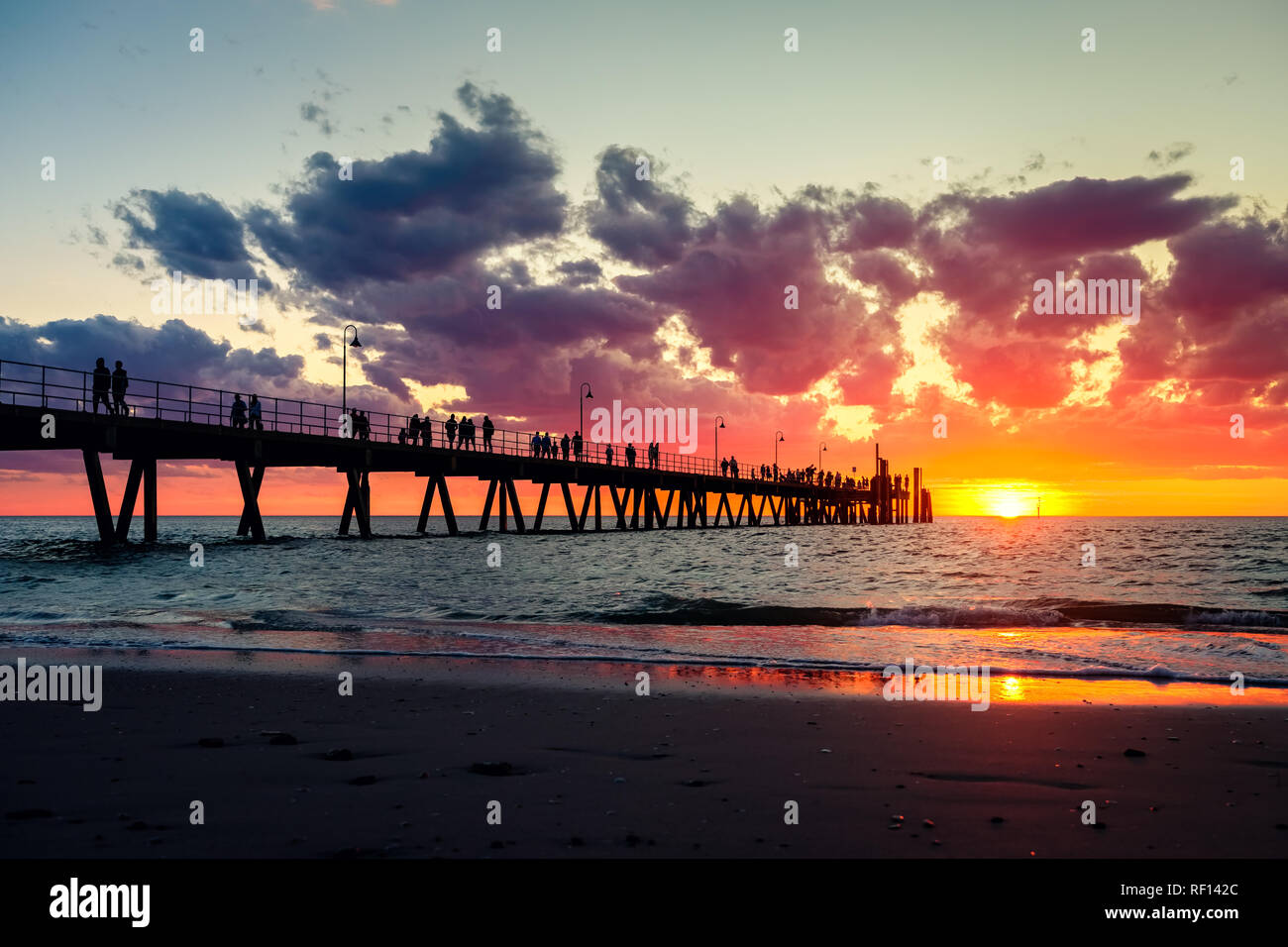 Menschen zu Fuß entlang Glenelg Pier während der dramatischen Sonnenuntergang in South Australia Stockfoto