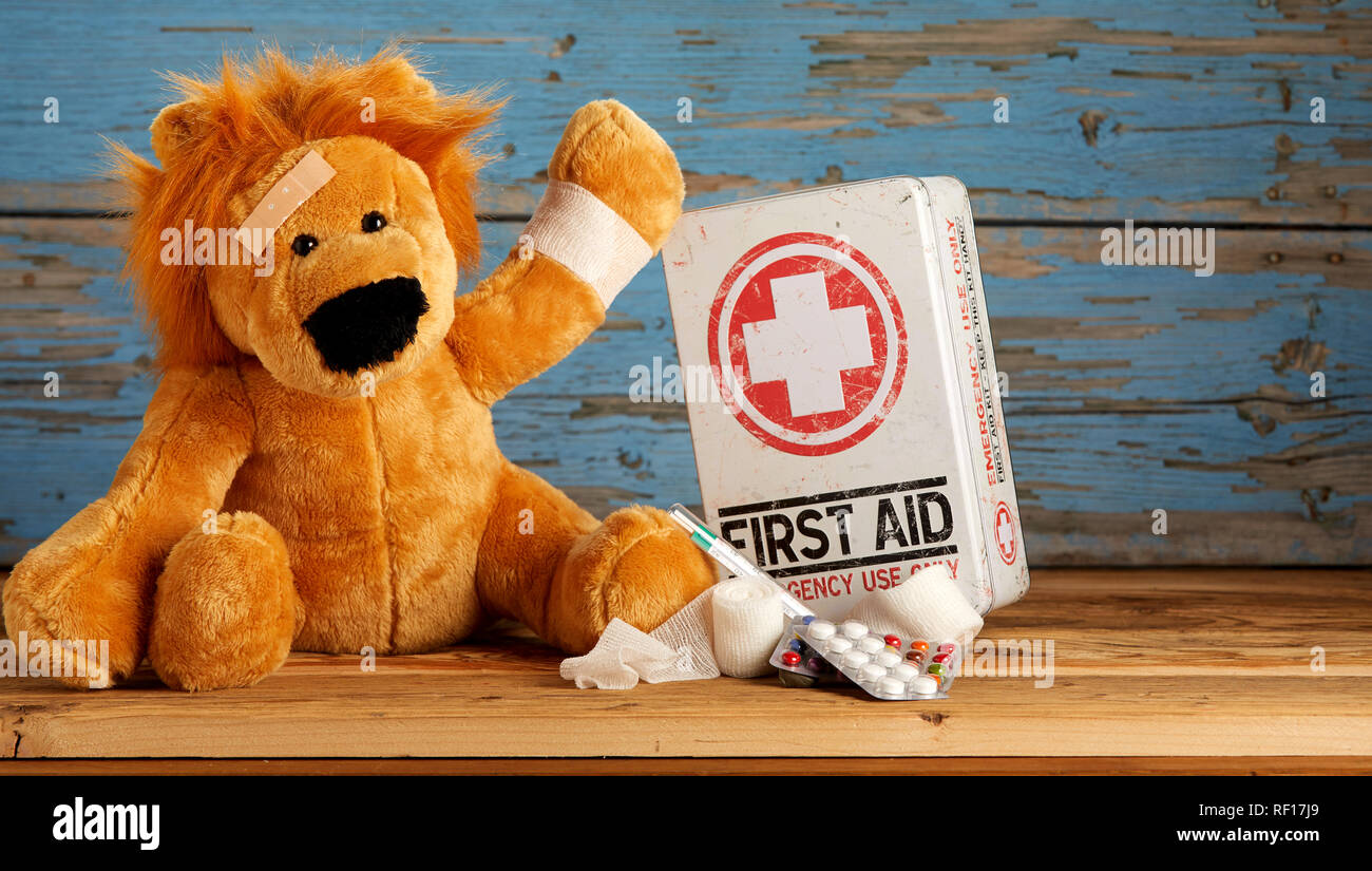 Veterinärmedizin von Kind Konzept mit einem niedlichen kleinen ausgestopften Löwen mit einem bandagierten Arm neben einer Erste Hilfe Kit im rustikalen, mit Holz mit kopieren Stockfoto