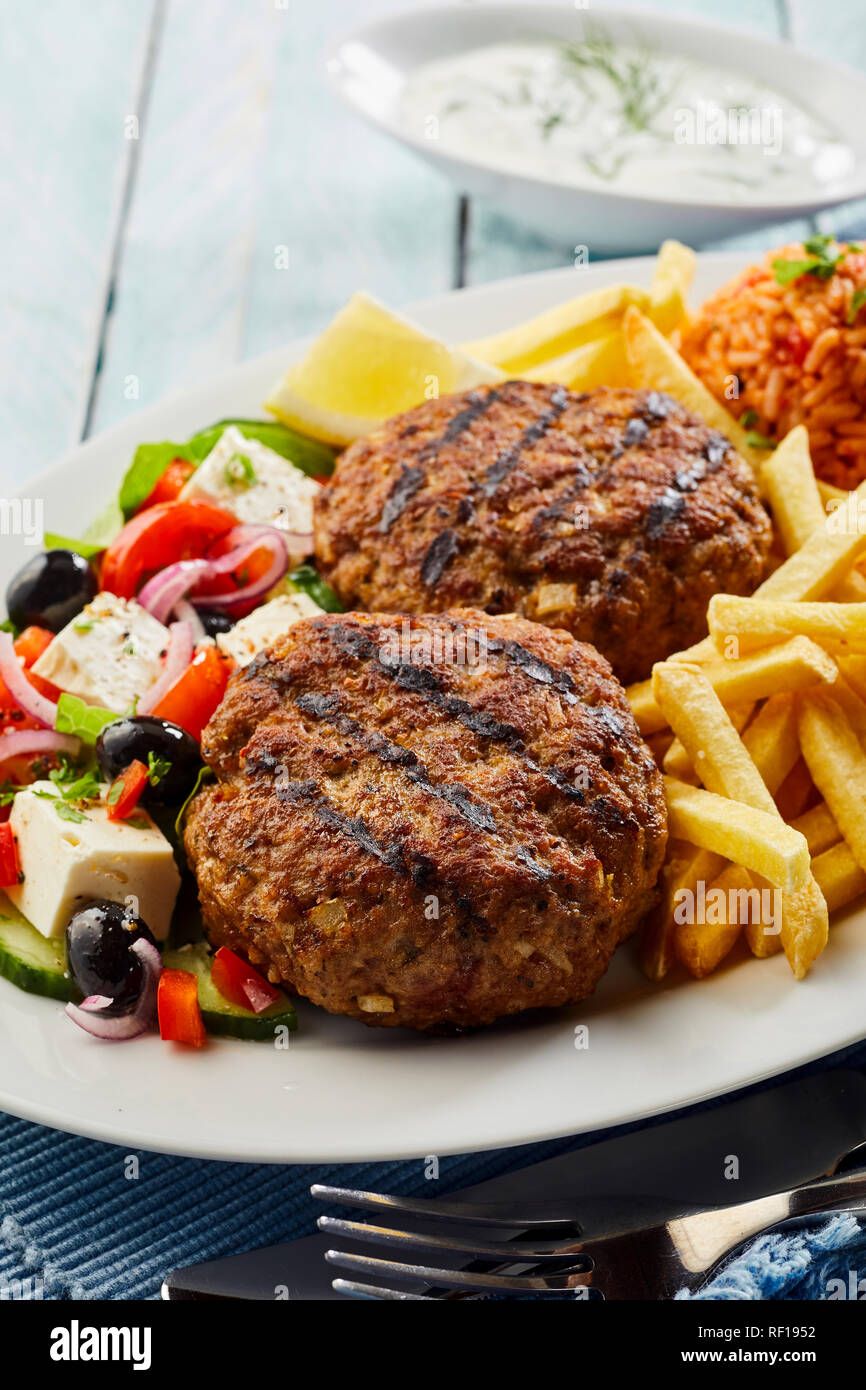 Würzige Bifteki, frikadelle oder frikkadel Frikadellen mit Hackfleisch/Faschiertes Rind- und Lammfleisch mit griechischen Salat und Pommes frites serviert. Stockfoto