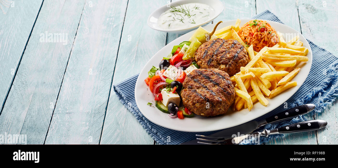 Bifteki, oder griechische Frikadellen, mit Salat, Tomate, Reis Pilav und fried Potato Chips auf einer ovalen Platte mit raita Dressing auf die Seite und kopieren Sie die Datei i Stockfoto