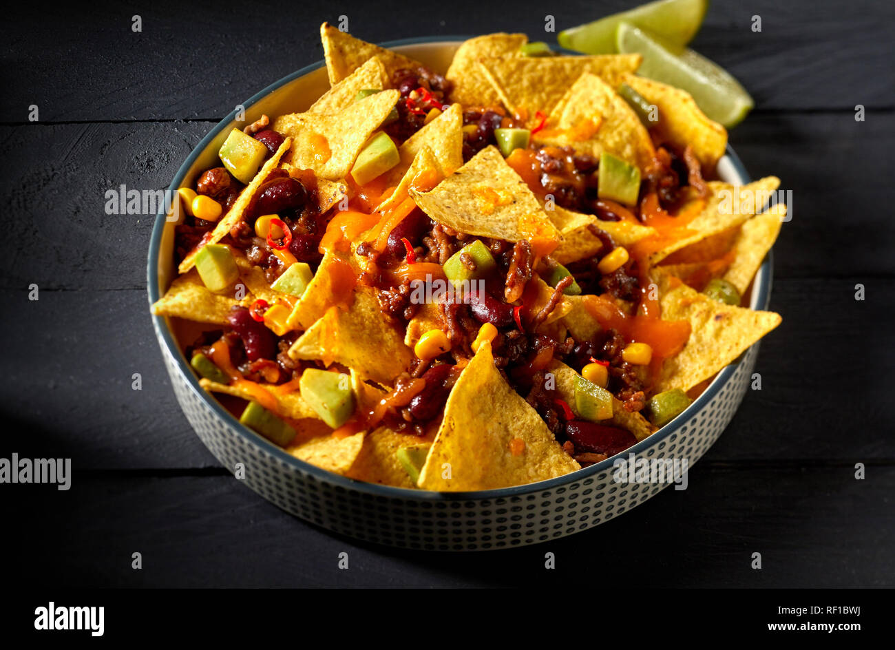 Chili con carne mit mexikanischen Tortillas oder Nachos mit Käse überbacken  mit gewürfelt frischer Avocado im Ofen gebacken und serviert mit Zitrone  auf einer dunklen backgr Stockfotografie - Alamy