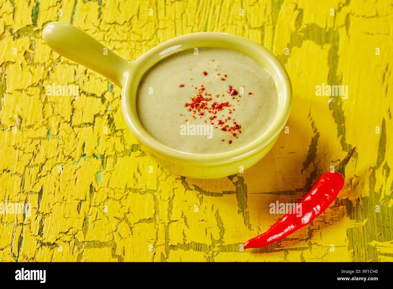Schüssel mit Guacamole avocado pear Dip garniert mit Chilipulver und eine frische ganze Cayenne chili Pod neben auf einem farbenfrohen texturierte Gelb zurück Stockfoto