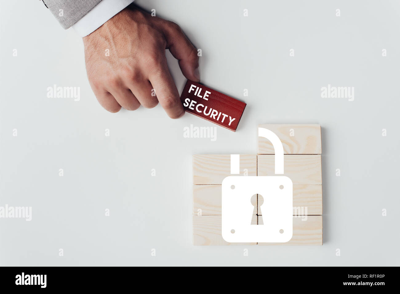 Teilansicht der Mann mit Ziegel mit 'File Security'-Schriftzug über Holzblöcke mit Schlosssymbol isoliert auf weißem Stockfoto