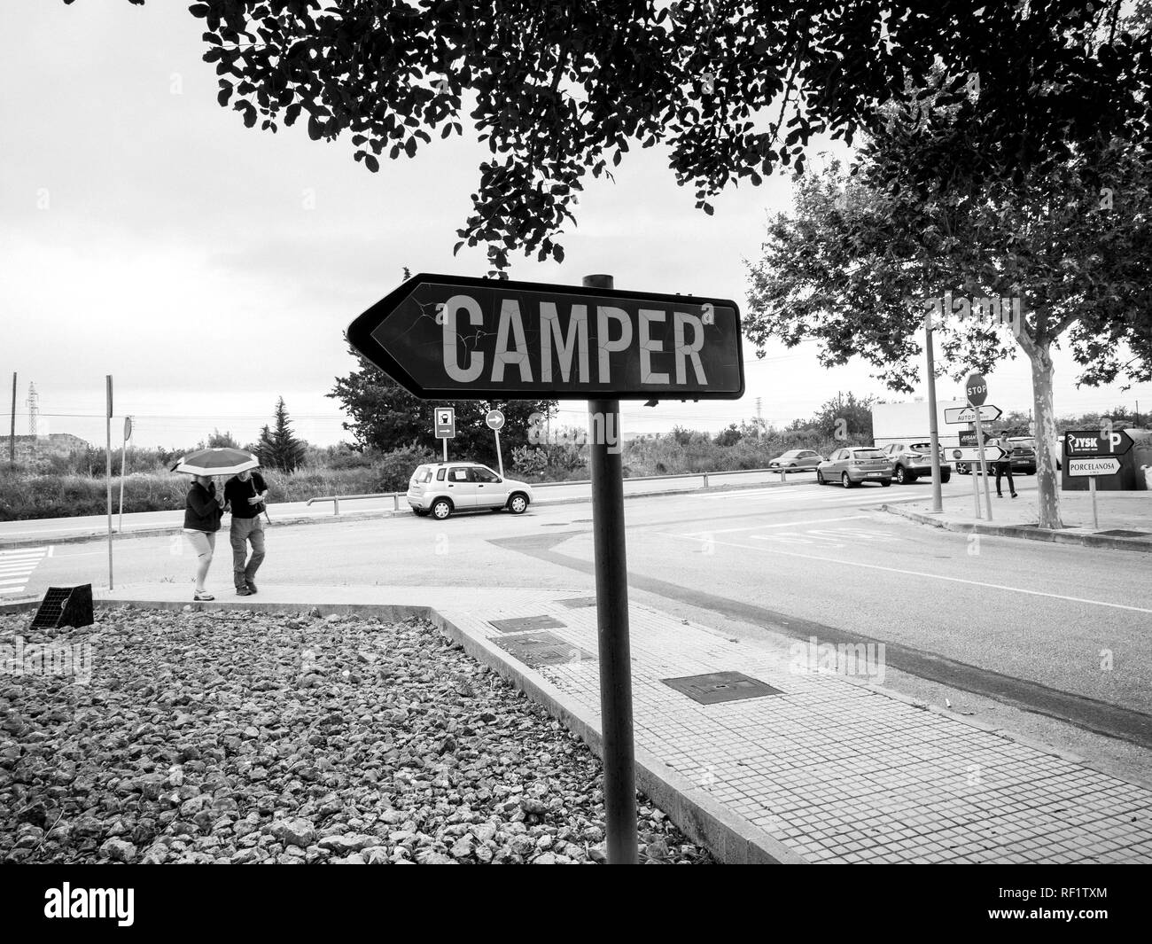 INCA, PALMA DE MALLORCA, SPANIEN - 8. Mai 2018: Paar für Camper Schuhfabrik Hauptsitz in Inca mit Schriftzug auf totem Pfeil Verkehrsschild - Schwarz und Weiß Stockfoto