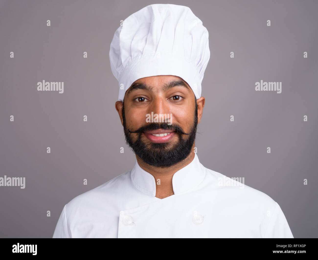Junge glücklich Inder Koch gegen grauer Hintergrund Stockfoto