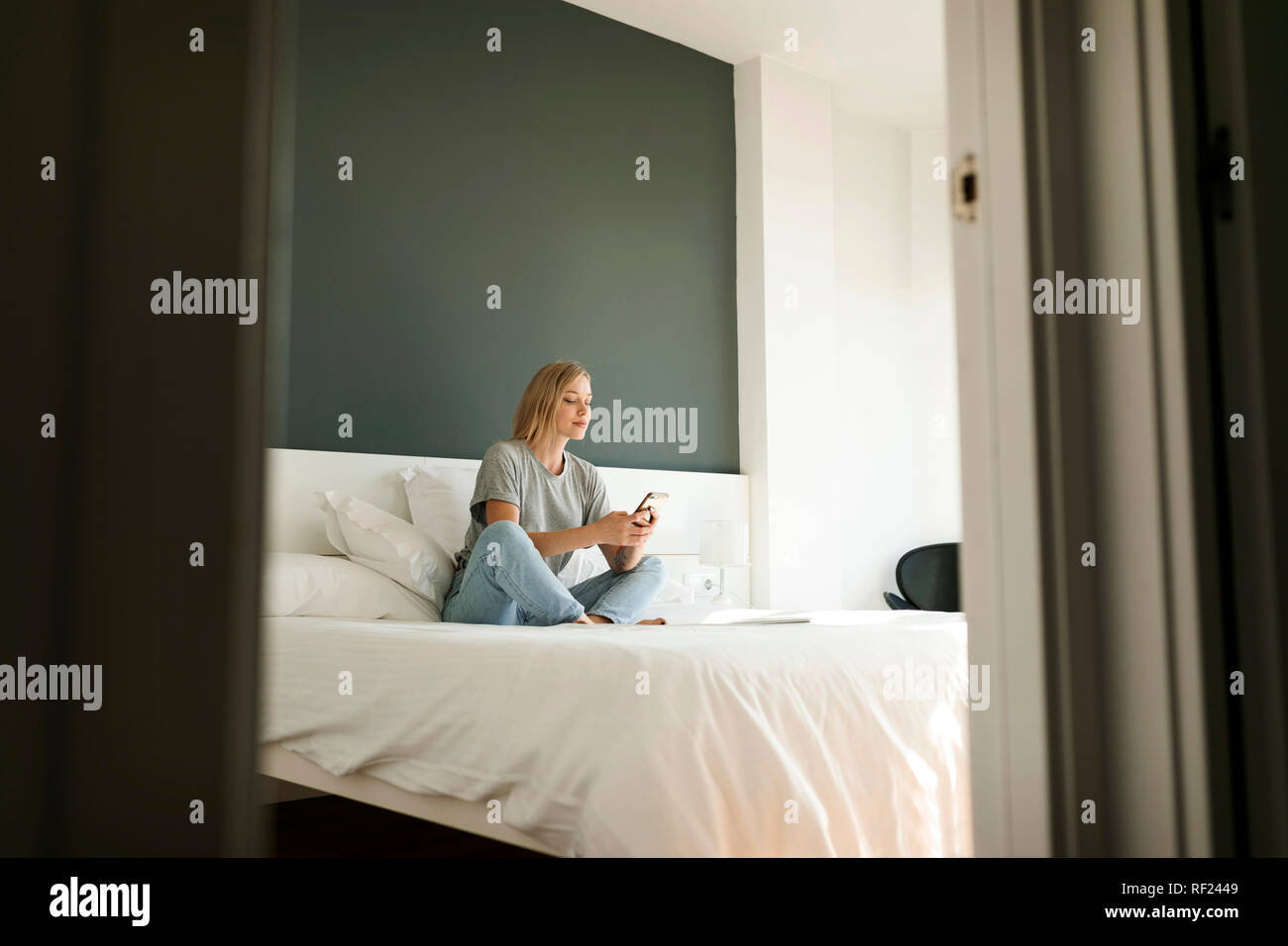 Junge Frau sitzt auf Bett mit Handy Stockfoto