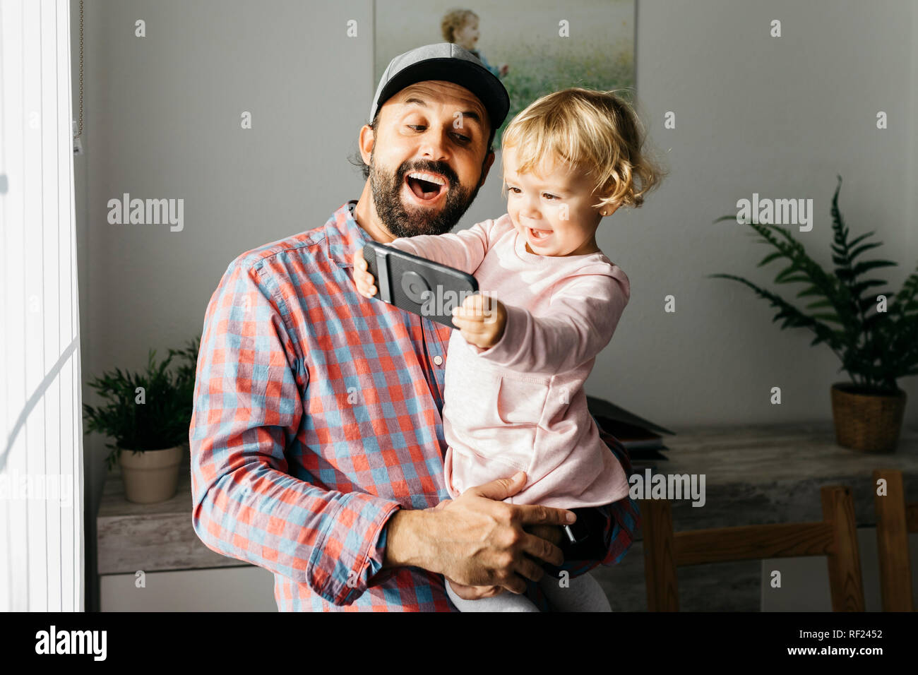 Vater, der seine kleine Tochter auf den Arm und spielte mit seinem Smartphone Stockfoto