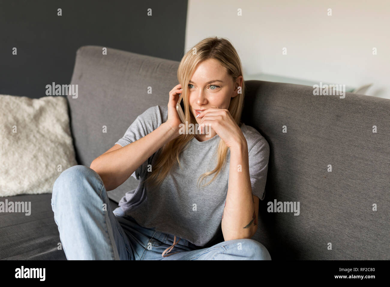 Lächelnde junge Frau sitzt auf der Couch Gespräch am Handy Stockfoto