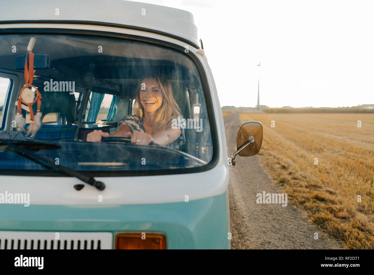 Glückliche junge Frau, die mit ihrem Wohnmobil ganz in ländlichen Landschaft Stockfoto