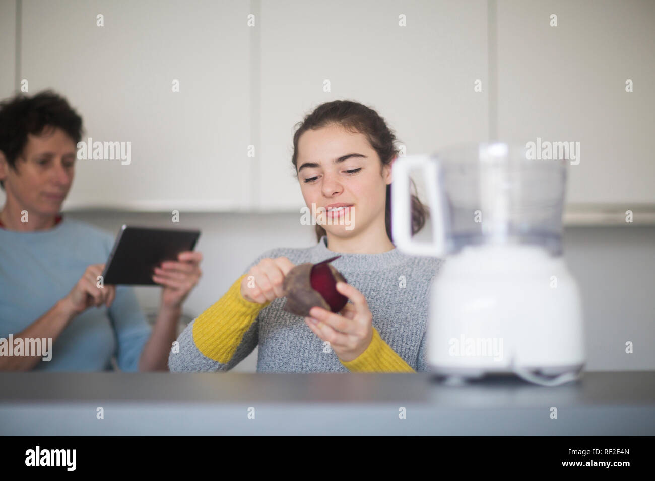 Portrait von lächelnden jungen Frau peeling Rote Bete in der Küche, während Mutter mit Tablet-PC im Hintergrund Stockfoto