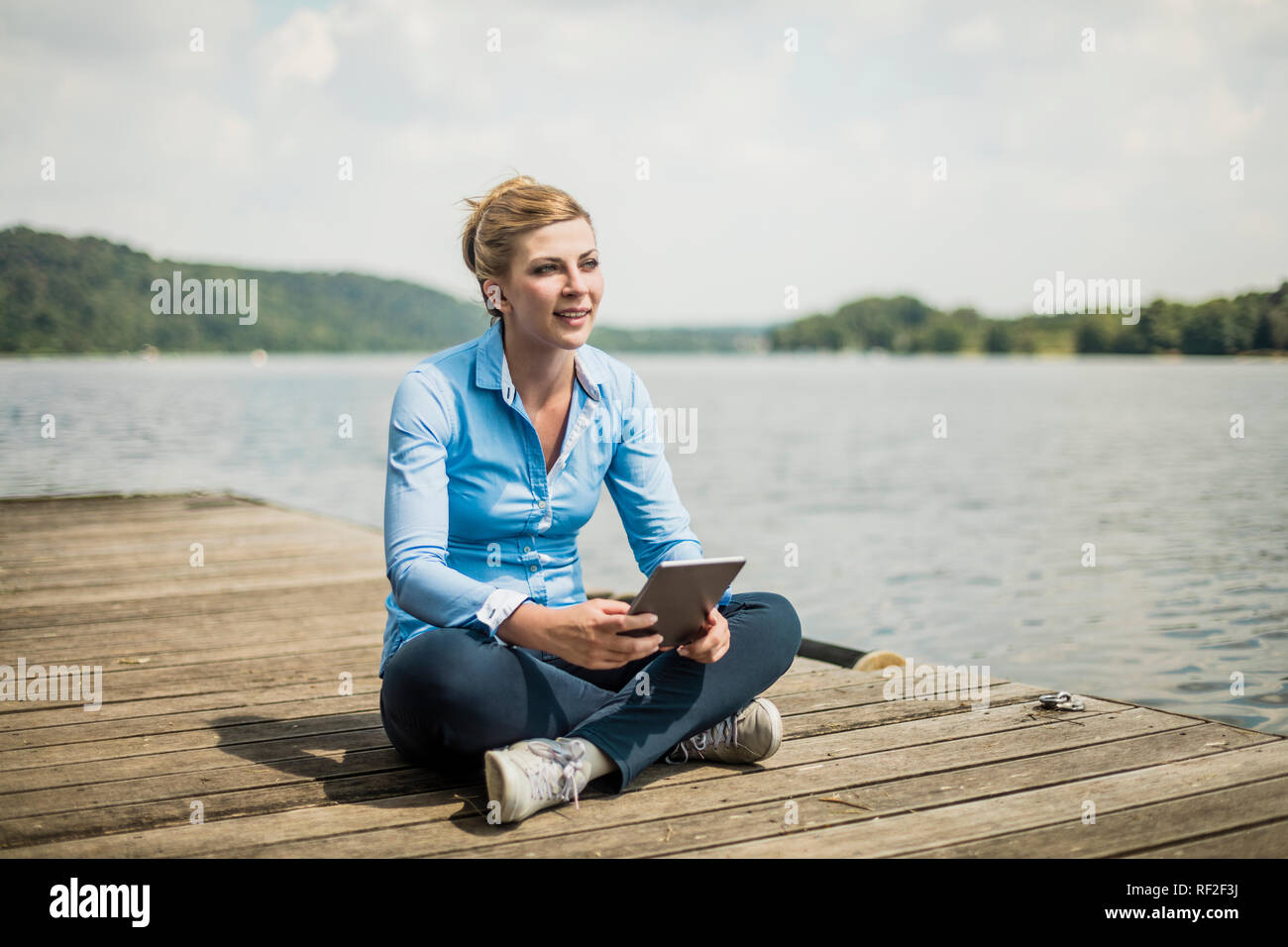 Frau sitzt auf der Jetty an einem See mit Tablet Stockfoto