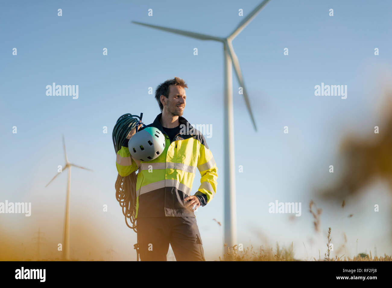 Techniker stehen ein Feld an einem Windpark mit Kletterausrüstung Stockfoto