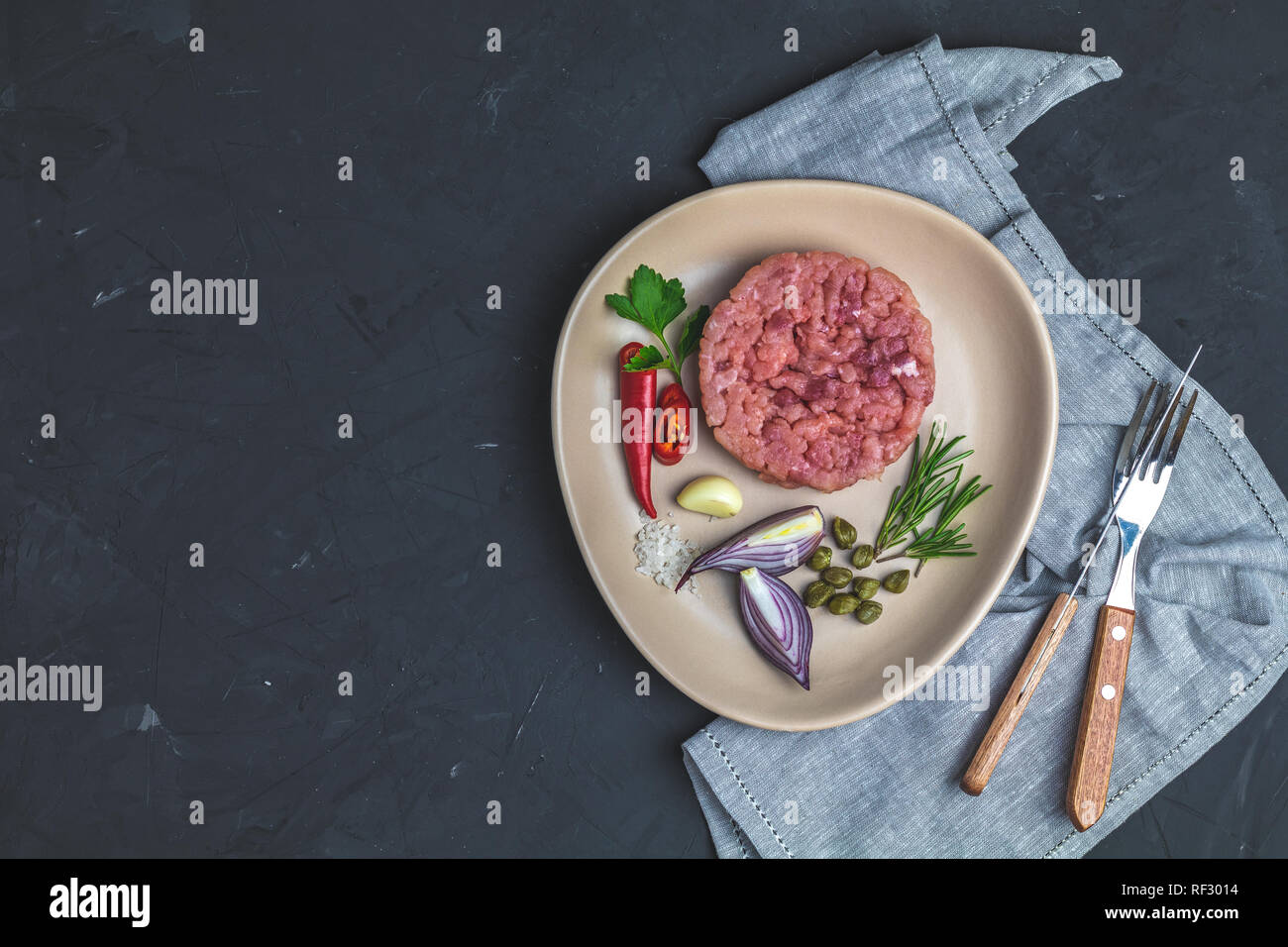 Lecker Steak tartare und Zutaten auf Keramik Teller, Besteck Messer, Gabel auf schwarzen Stein Beton texturierte Oberfläche Hintergrund. Platz kopieren Stockfoto