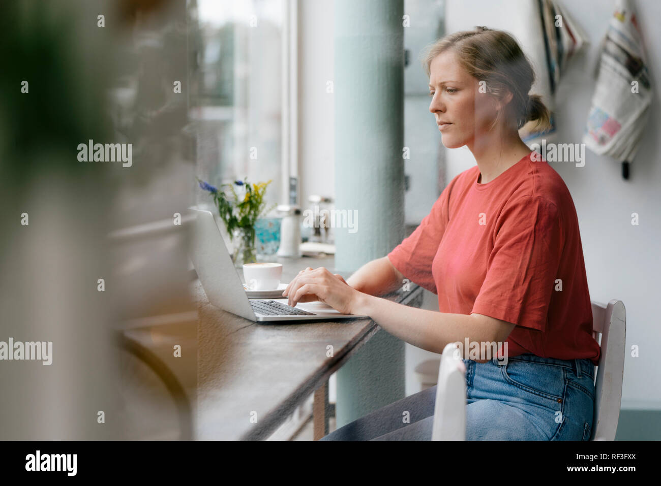 Junge Frau mit Laptop am Fenster in einem Cafe Stockfoto
