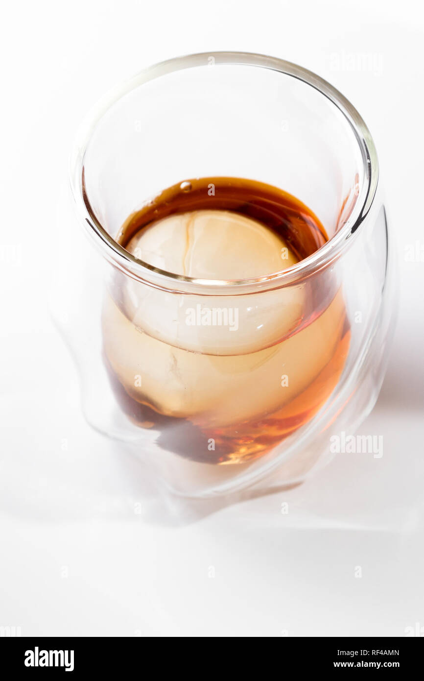 Bourbon serviert in einem doppelwandigen Whisky Glas mit Eis Kugel über einen weißen Hintergrund serviert. Stockfoto