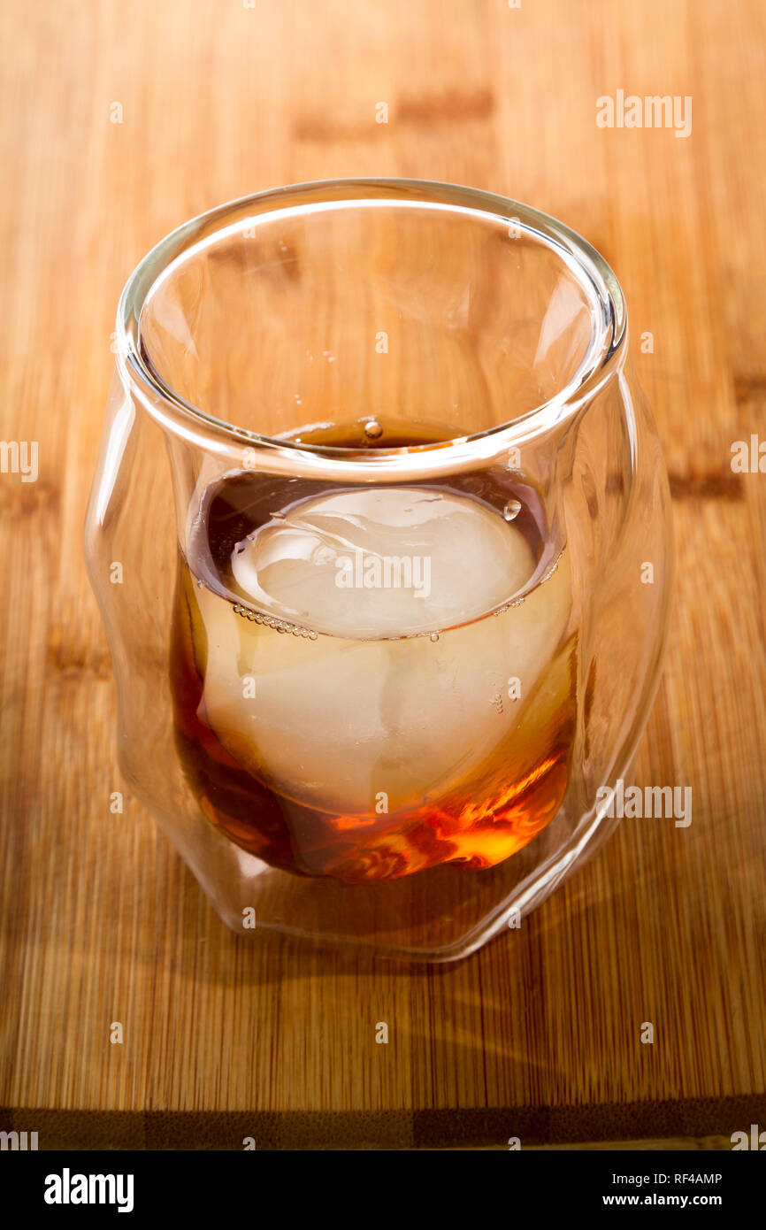 Gerade Whiskey serviert in einem doppelwandigen Whisky Glas serviert mit einem Eis Kugel auf einer hölzernen Balken oben serviert. Stockfoto