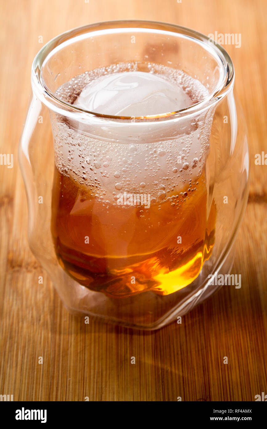Whiskey Soda serviert in einem doppelwandigen Whisky Glas serviert mit einem Eis Kugel auf einer hölzernen Balken oben serviert. Stockfoto