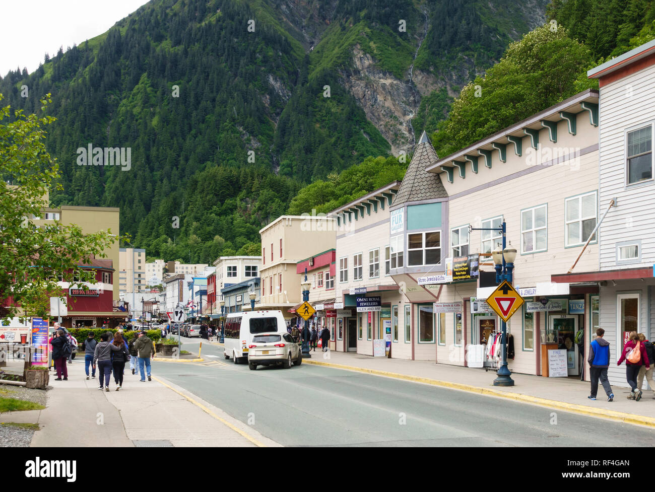 Touristen und Ausflügler besuchen Sie Geschäfte und Läden entlang der Franklin Street in der Innenstadt von Juneau, Alaska. Steile Berghänge bieten eine dramatische Kulisse. Stockfoto