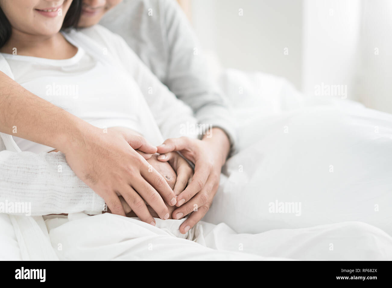 Zugeschnittenes Bild der schönen schwangeren Frau und ihrem stattlichen Mann umarmen den Bauch. Liebe Paar Hände machen ein Herz auf den schwangeren Bauch. Stockfoto
