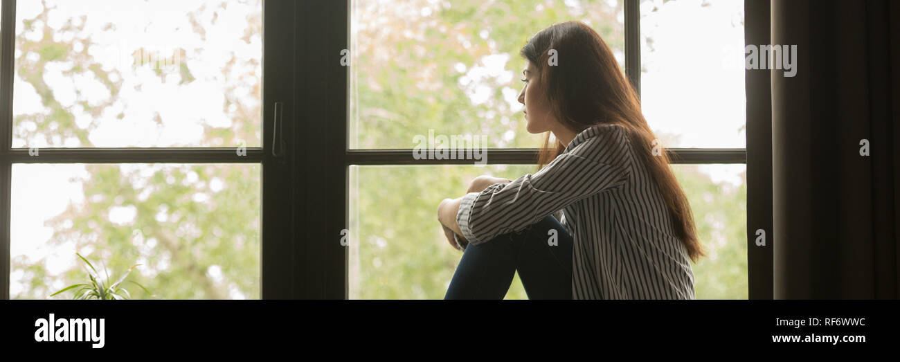 Traurige junge Frau sitzt auf der Suche Fenster und Denken Stockfoto