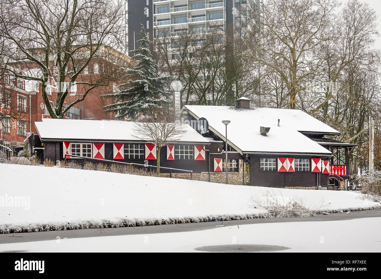 Rotterdam, 22. Januar 2019: Verschneite "Swiss Chalet", jetzt ein türkisches Restaurant, in die winterliche Landschaft des Parks, mit modernen Hochhaus in der Stockfoto