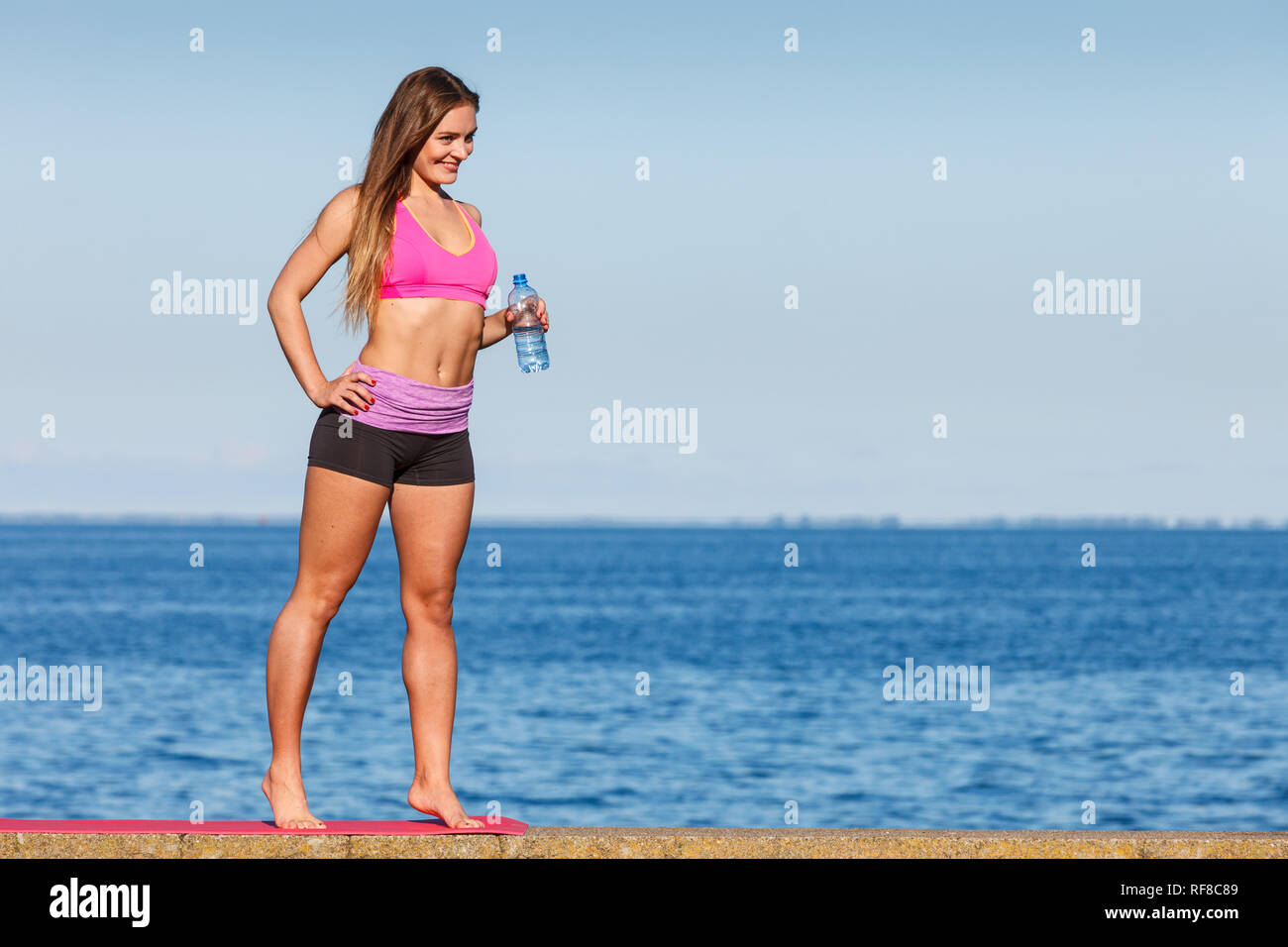 Frau in Sportswear nimmt einen Bruch von Trinkwasser aus Kunststoff Flasche zu rehydrieren, Erholung nach dem Sport Training Outdoor von Seaside Stockfoto