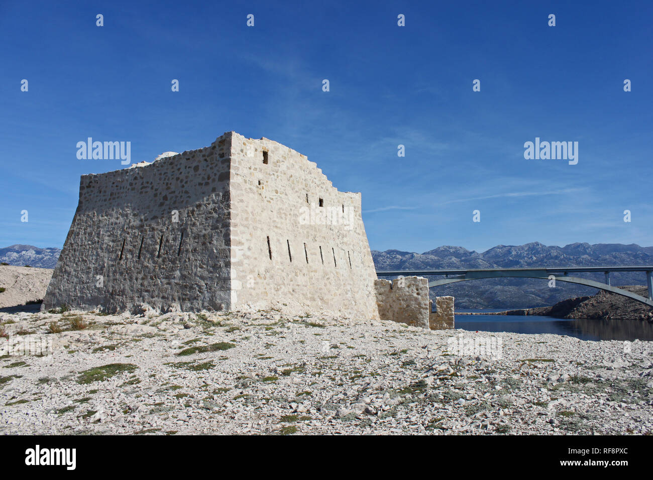 Ruinen der alten Festung Fortica auf der Insel Pag (Kroatien). Die Brücke verbindet die Insel mit dem Land im Hintergrund. Stockfoto