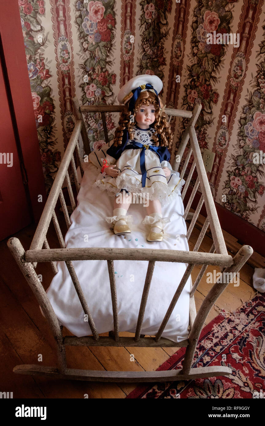 Vintage baby doll Bett mit antiken Puppe mit Red Victorian locken in Sailor kleid und hut. Satin Schuhe mit rüschen Socken, Vintage viktorianische Tapeten. Stockfoto