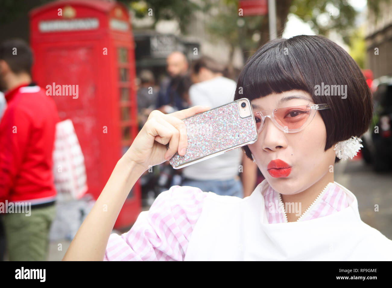 LONDON, Großbritannien - 14 September 2018: Leute auf der Straße, während der London Fashion Week. Chinesische Blogger in einer weißen Bluse und Rock mit roten Beutel in Pol Stockfoto