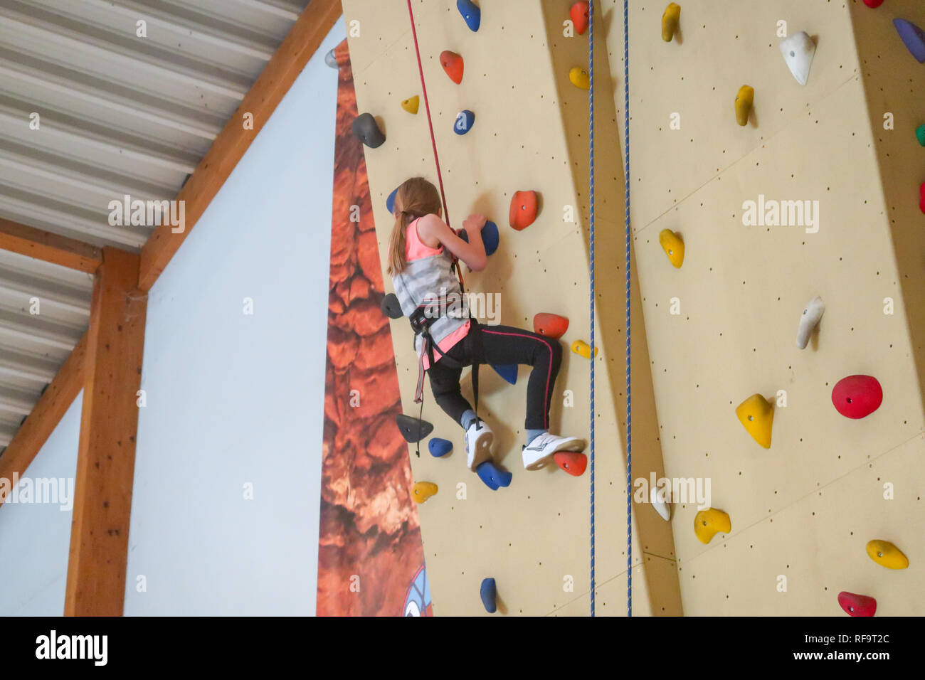 Ein 9 Jahre altes Mädchen klettert eine Kletterwand in einem Überhang Stockfoto