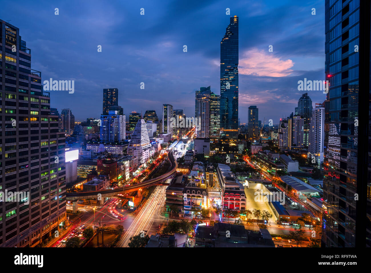 Bangkok, 12.11.18: Stadtbild der berühmten Maha Nakhon Tower in Bangkok, Thailand. Leichte Wanderwege in den Straßen von den Autos. Schönen Sonnenuntergang in den Himmel hinter Türme der Stadt. Stockfoto