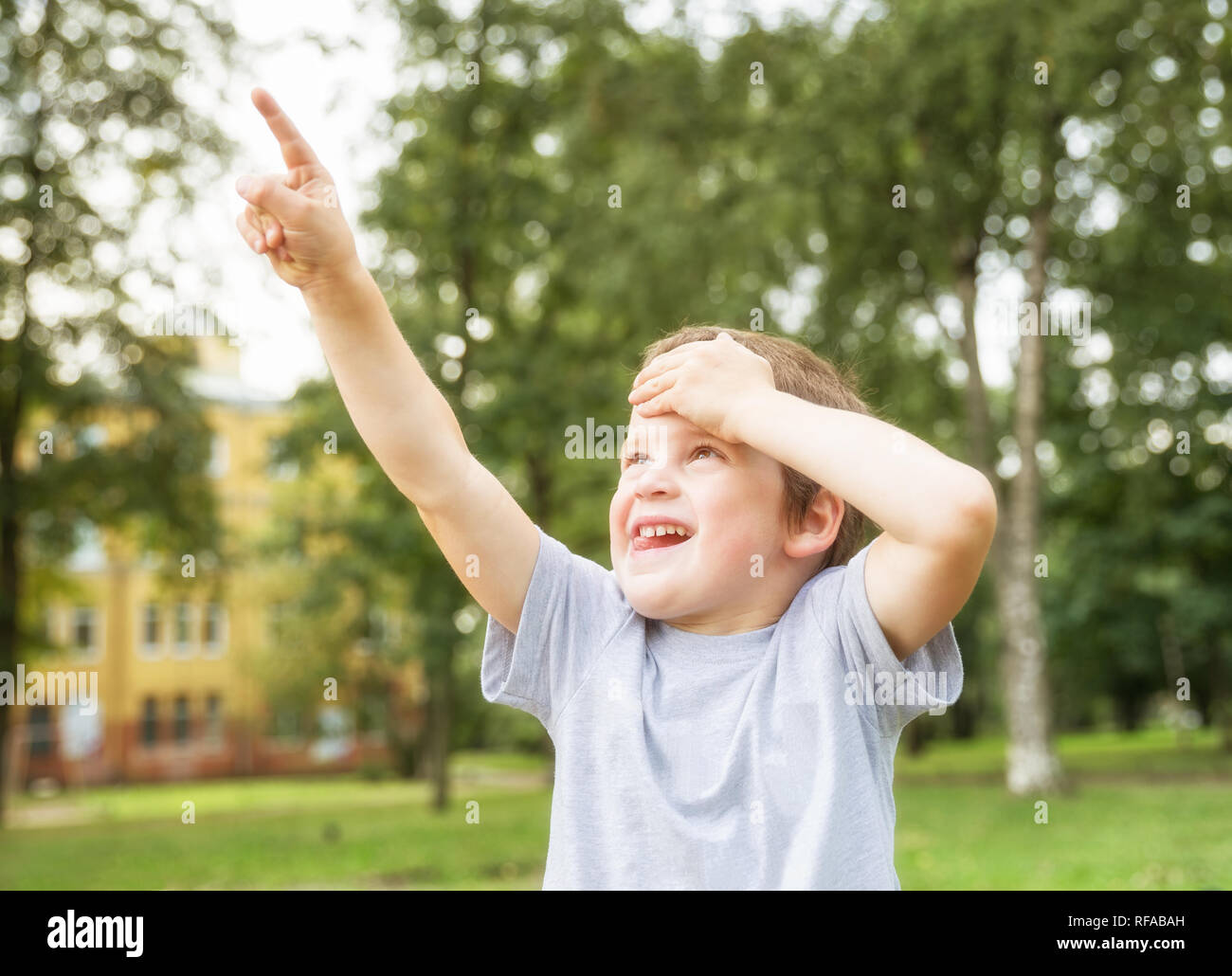 Junge 5 Jahre alt sucht etwas und zeigt mit dem Finger in Sommer Park auf dem Hintergrund der Bäume Stockfoto