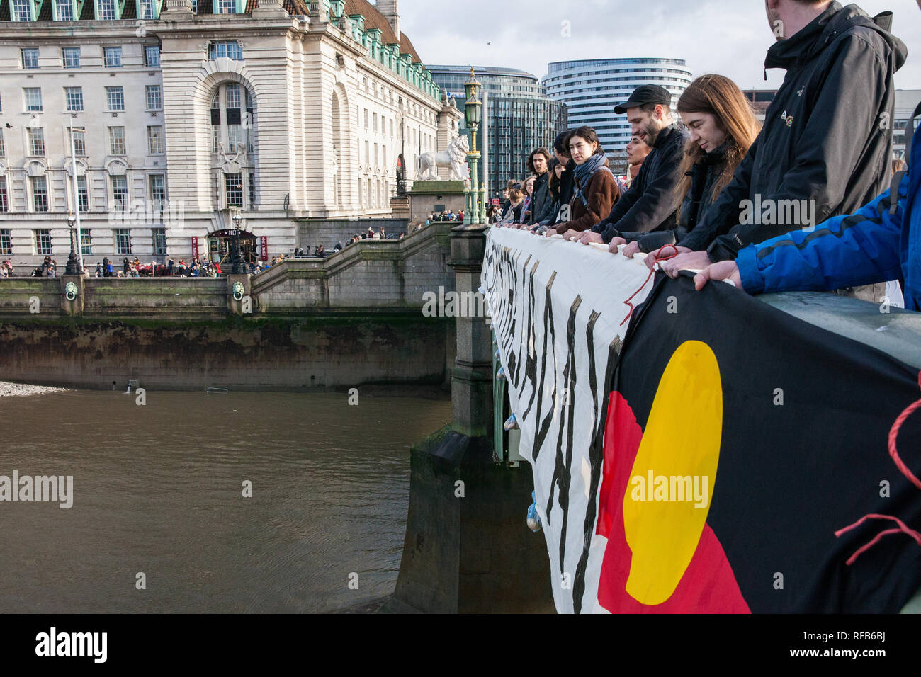 London, Großbritannien. 25. Januar, 2019. Aktivisten drop ein Banner und ein aborigine Flagge von Westminster Bridge, im Blick auf die Häuser des Parlaments, für die Abschaffung von Australien Tag der Kundgebungen in jedem australischen Stadt morgen an. Die Veranstaltung wurde in Solidarität mit den Aborigines und Torres Strait Islander Wer Australien Tag, ein Tag feiert die Besiedlung von Australien, ein Tag der Trauer eher als ein Tag der Feier werden organisiert. Credit: Mark Kerrison/Alamy leben Nachrichten Stockfoto