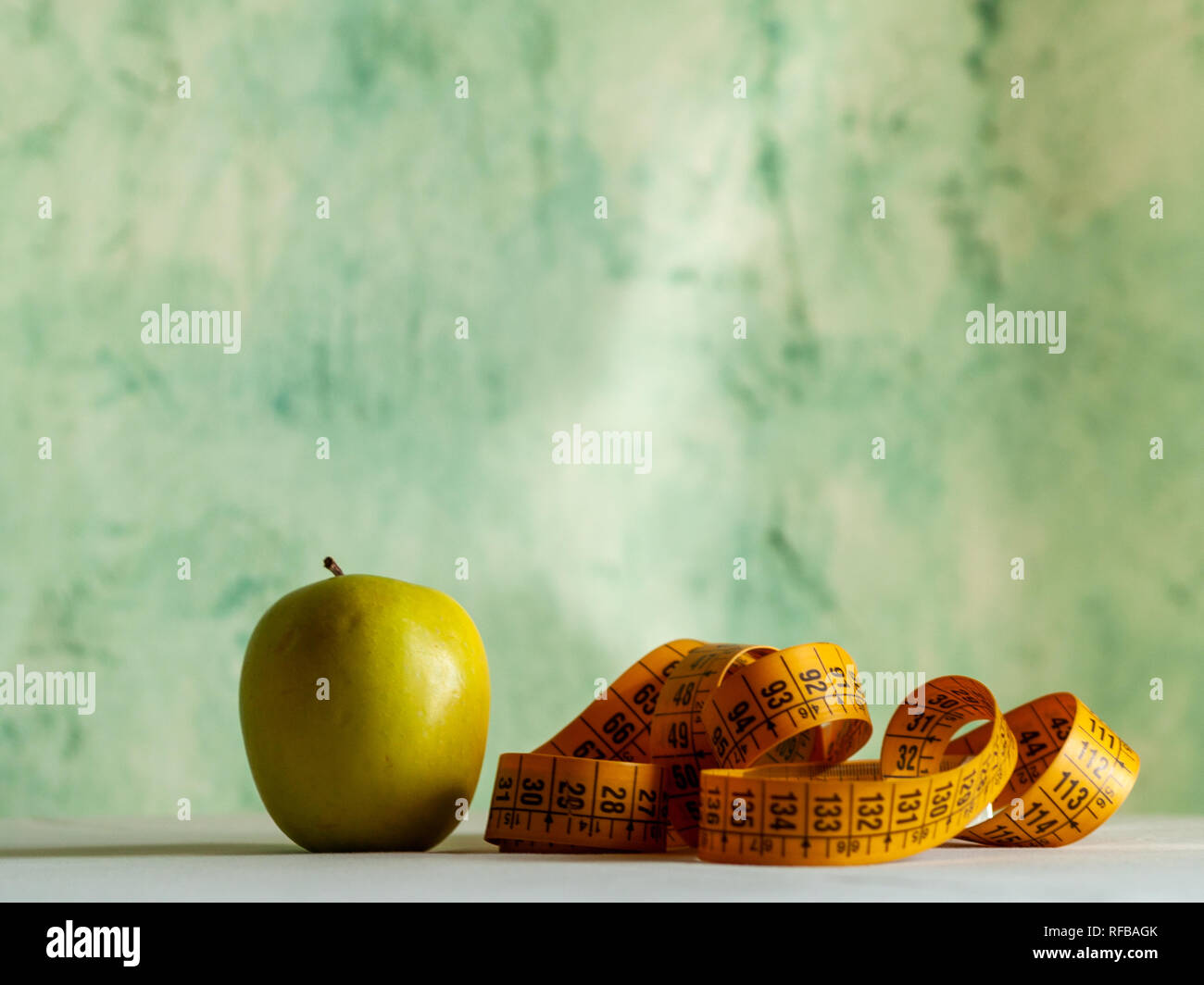 Adipositas Konzept. Ein grüner Apfel und ein Maßband auf einem Tisch Stockfoto