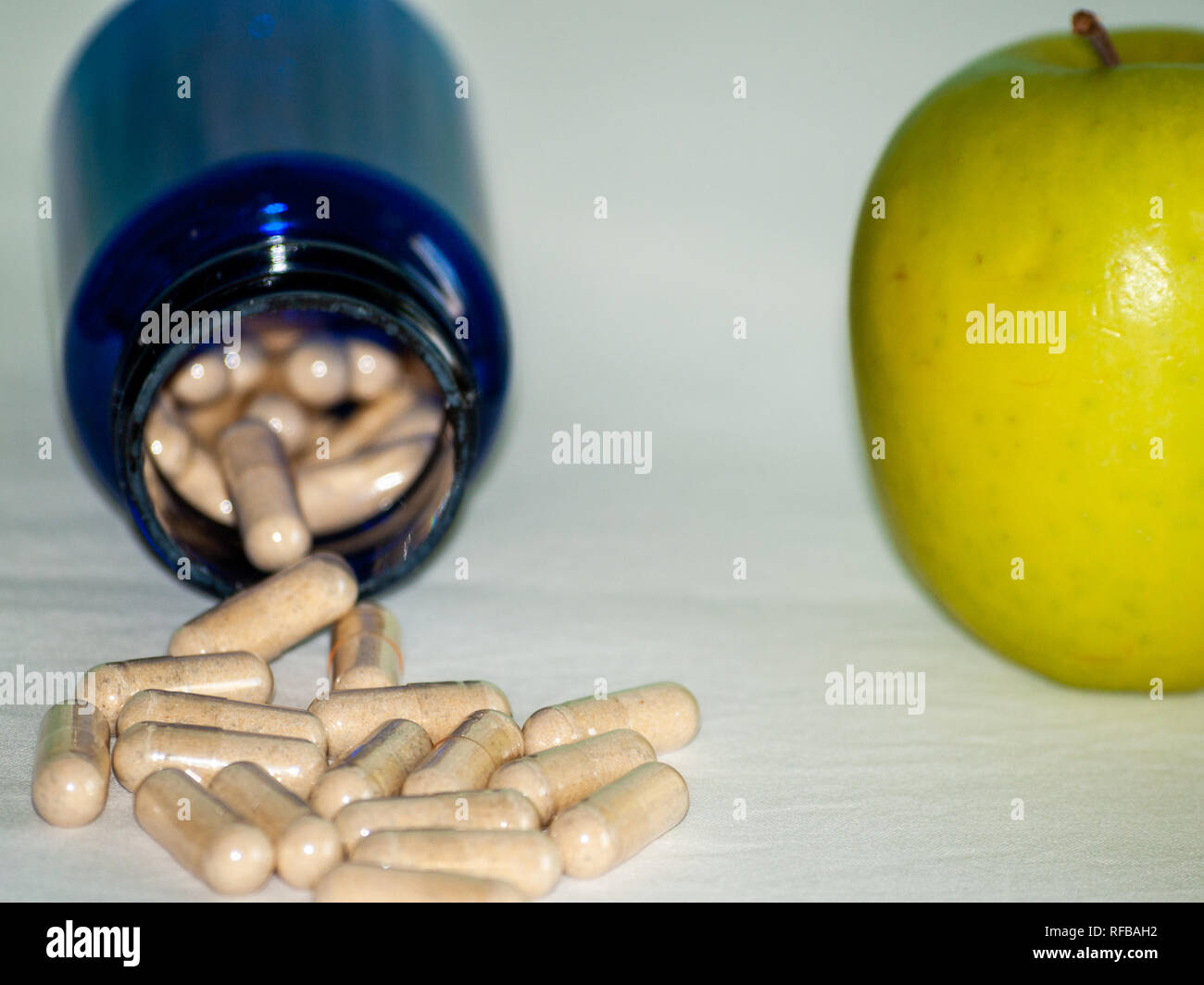 Einen Apfel und eine blaue Container mit pflanzenfasern Pillen auf einem Tisch Stockfoto