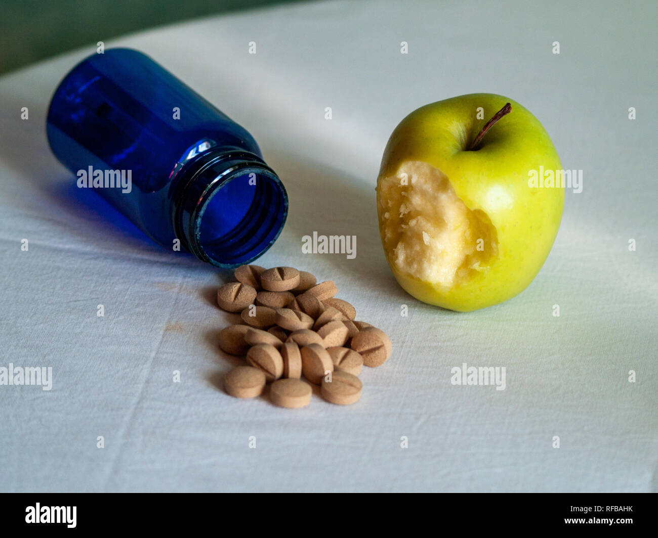 Eine gebissen Apple und einem blauen Container mit pflanzenfasern Pillen auf einem Tisch Stockfoto