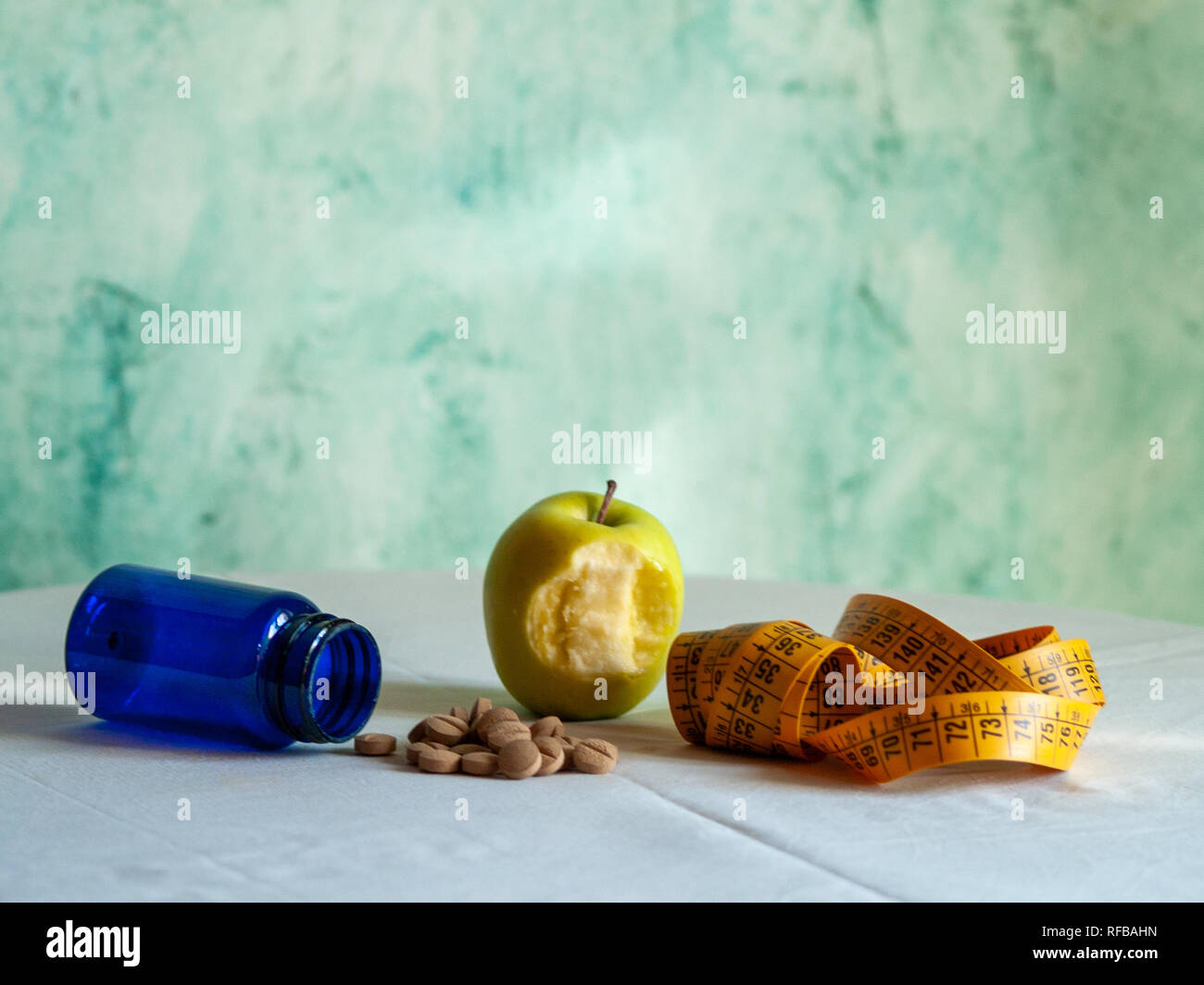 Eine gebissen Apple, ein Maßband und einem blauen Container mit pflanzenfasern Pillen auf einem Tisch Stockfoto