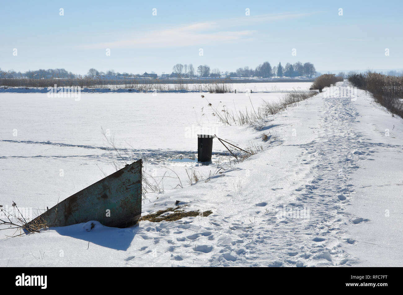 Winter Szene mit alten rostigen Boot am Ufer des zugefrorenen See in sonniger Tag, schneebedeckten Landschaft mit Fußspuren auf dem Weg Stockfoto