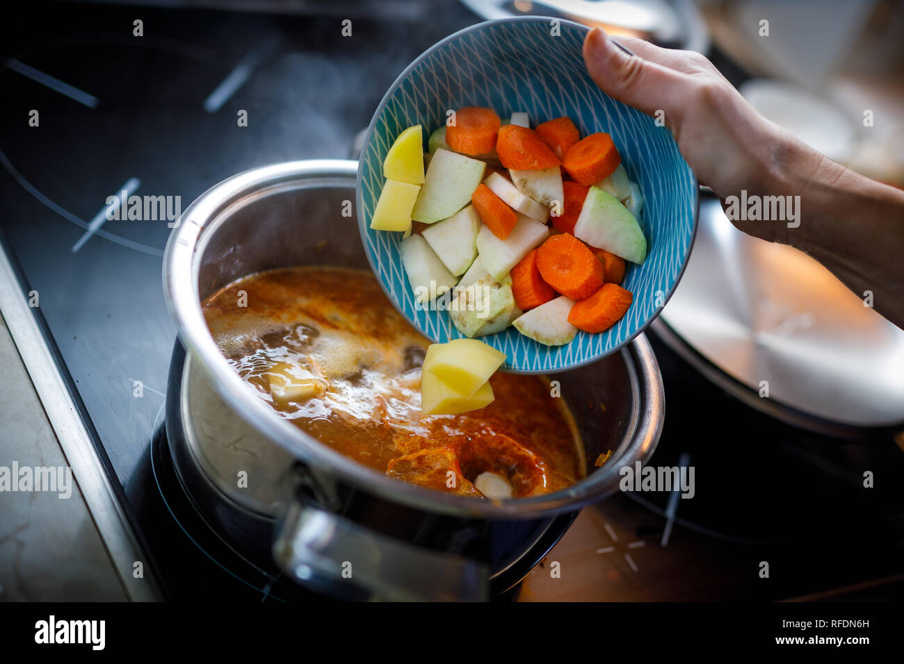 Das zerkleinerte Gemüse in die kochende Gulasch Suppe im Topf gießen Stockfoto